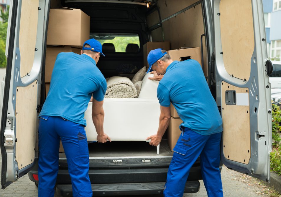 Two Male Workers In Blue Uniform Adjusting Sofa In Truck
